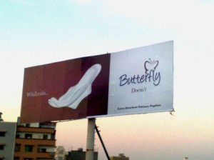 Werbeschild in Karachi - Links eine weiße Binde mit Flügeln vor rotem Grund und der Schrift: WikiLeaks - rechts weißer Hintergrund und rote Schrift: Butterfly Doesn't