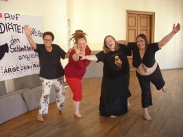 Vier Frauen der ARGE Dicke Weiber posieren beim Workshop für die Kamera, lachend und die Arme zur Kamera gestreckt, auf einem Bein stehend